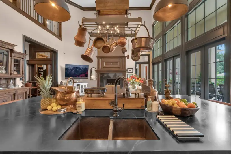 Kitchen island with a dark stone top, a copper sink, a copper pot rack, and black-framed doors.