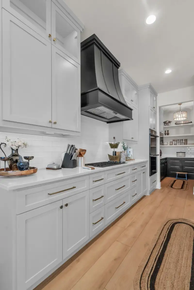 Kitchen with white shaker cabinets, a black range hood, a gas cooktop, and a pantry visible through a doorway.