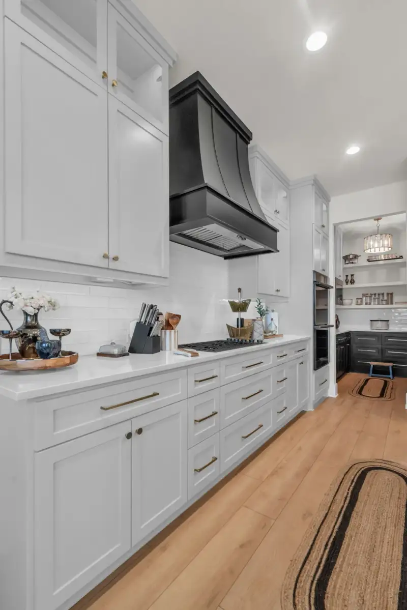 Kitchen with white shaker cabinets, a black range hood, a gas cooktop, and a pantry visible through a doorway.