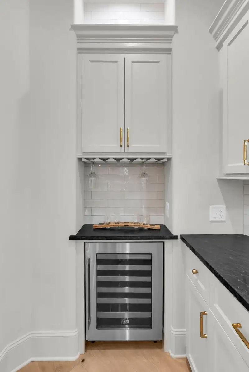Wine refrigerator below a cabinet with a stemware rack and a dark countertop.