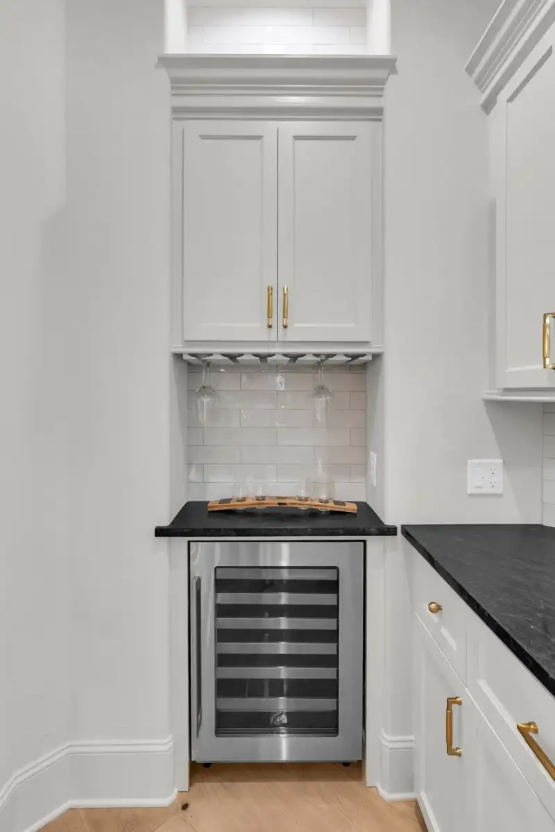 Wine refrigerator below a cabinet with a stemware rack and a dark countertop.