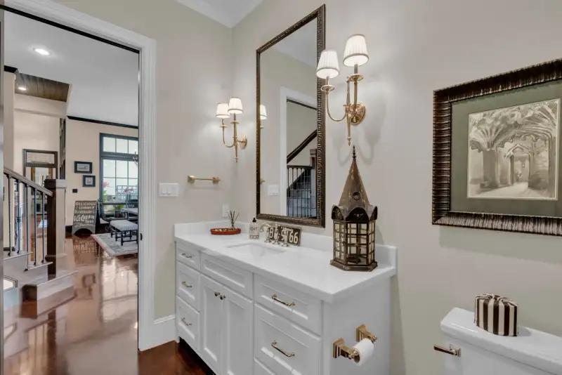 Powder room with a white vanity, a framed mirror, brass wall sconces, and a framed sketch.