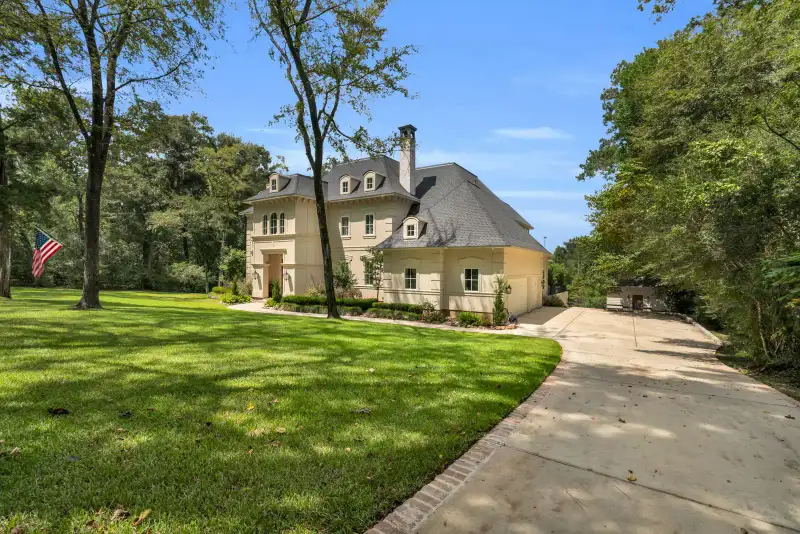 Cream stucco home seen across a broad front lawn, framed by mature trees and a concrete drive.