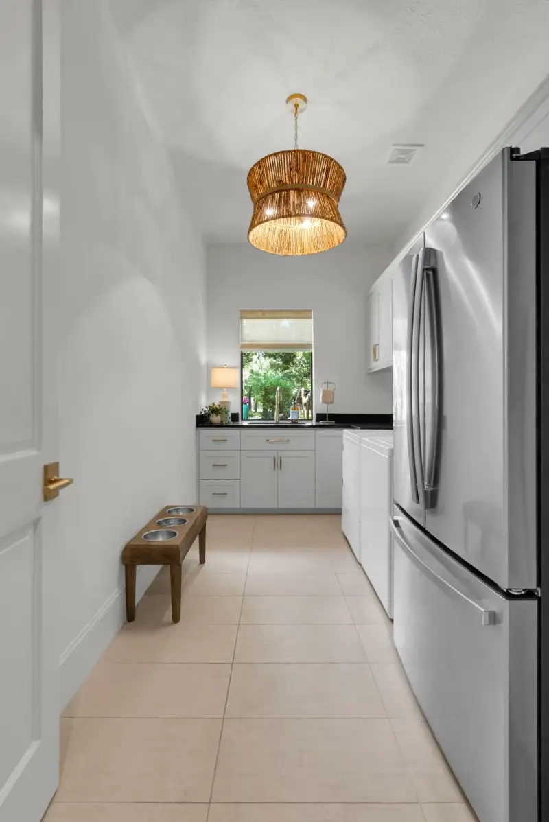 Laundry room with a woven pendant light, a pet bowl bench, a window over the sink, and a stainless refrigerator.