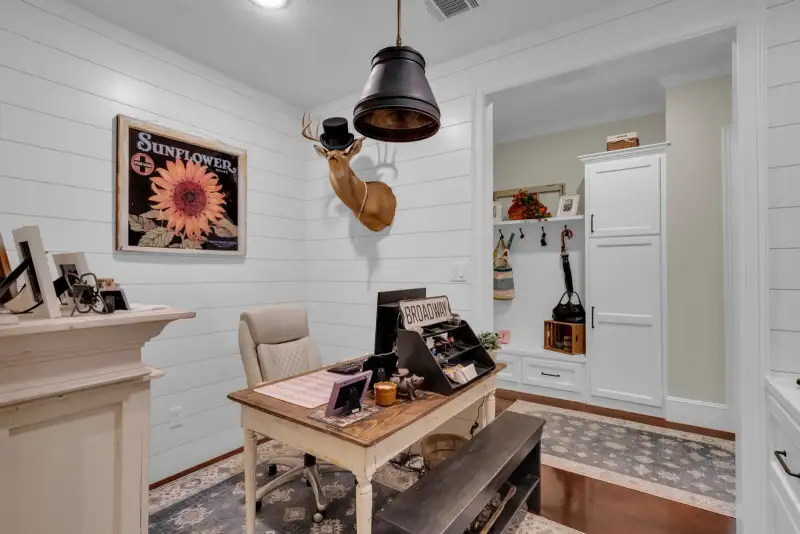 Home office with shiplap walls, a wood desk, a mounted deer head, and a white built-in cabinet wall.