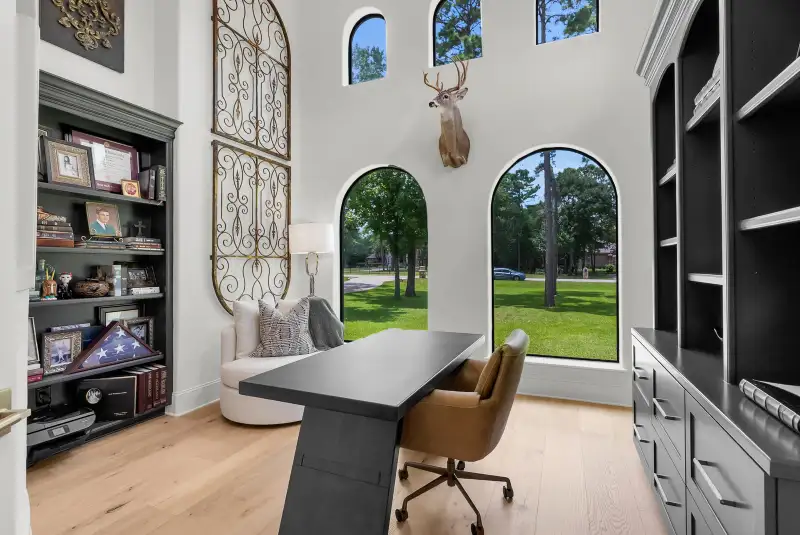 Study with arched windows, a dark desk, a leather chair, and a built-in bookcase with iron wall art.