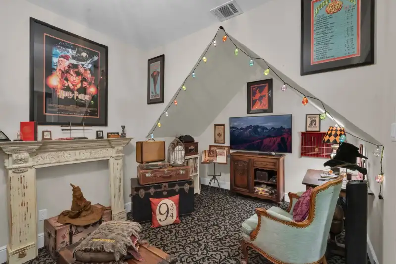 Sloped-ceiling room with string lights, a white fireplace mantel, a framed movie poster, and a wood trunk.