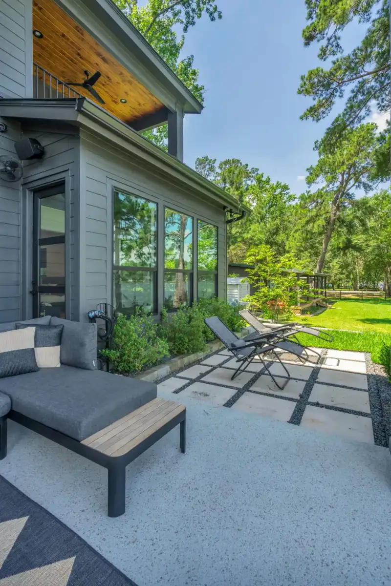 Side patio with a gray chaise lounge, a wood ceiling, and a lawn with trees beyond.
