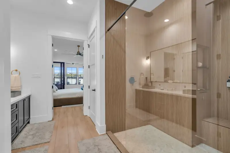 Bathroom with a glass-enclosed shower and a doorway into a bedroom with a ceiling fan.