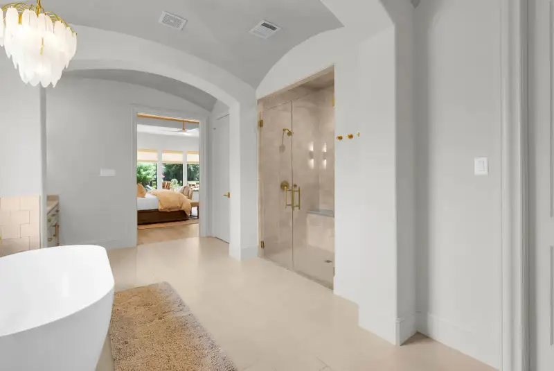 Primary bath with a freestanding tub, an arched hallway, and a glass-enclosed shower with brass fixtures.
