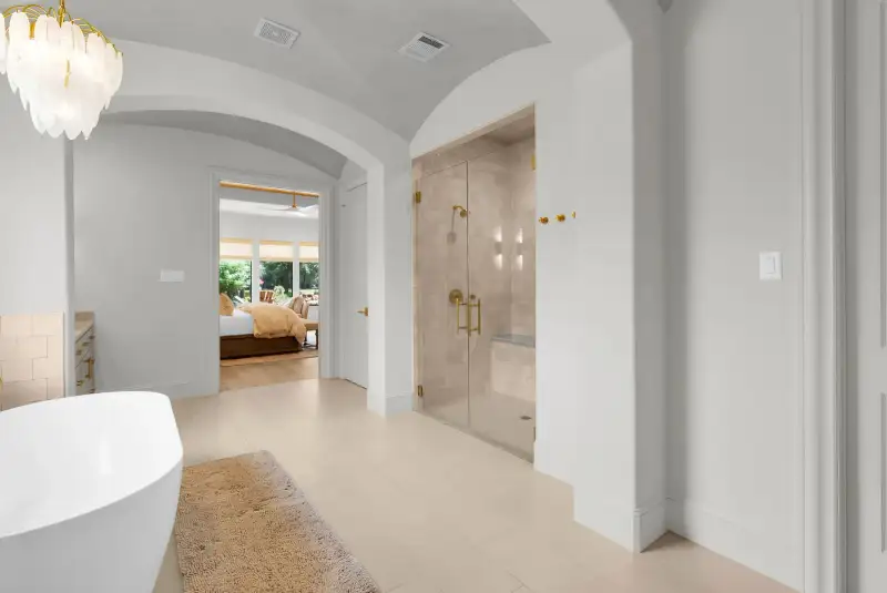Primary bath with a freestanding tub, an arched hallway, and a glass-enclosed shower with brass fixtures.