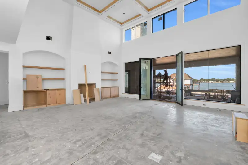 Two-story room with a coffered ceiling and glass doors open to a covered patio with a lake view.