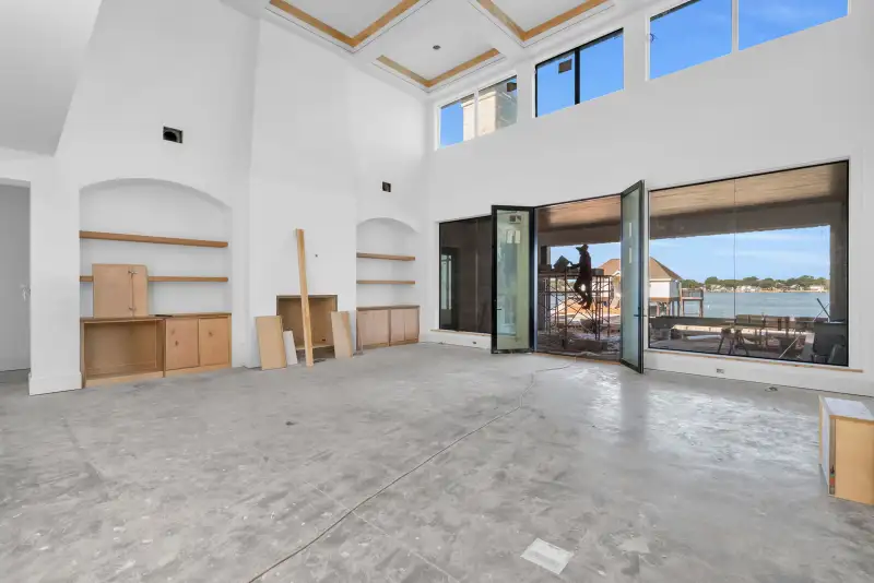 Two-story room with a coffered ceiling and glass doors open to a covered patio with a lake view.