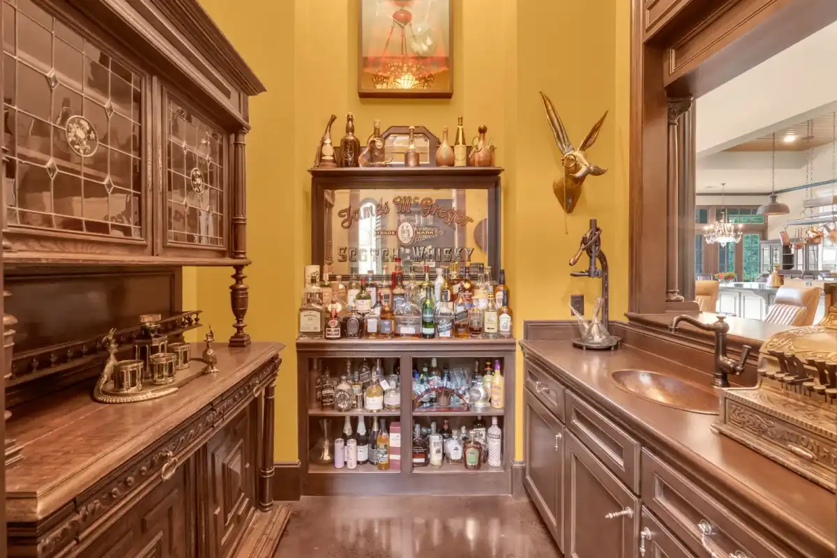 Wet bar with dark wood cabinetry, leaded glass doors, a bottle display, and a copper sink against gold walls.