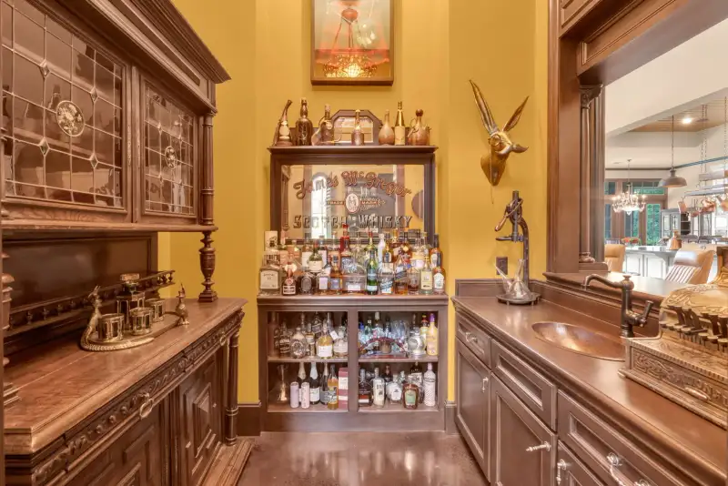 Wet bar with dark wood cabinetry, leaded glass doors, a bottle display, and a copper sink against gold walls.