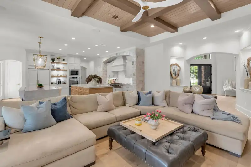 Open living area with a coffered wood ceiling, a sectional sofa, and a kitchen with a white range hood.