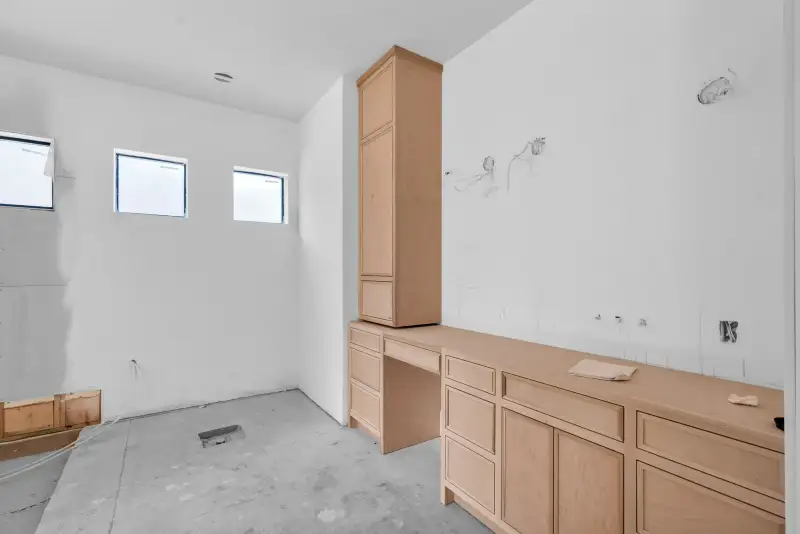 Unfinished room with light wood base cabinets, a tall cabinet, and three small high windows.
