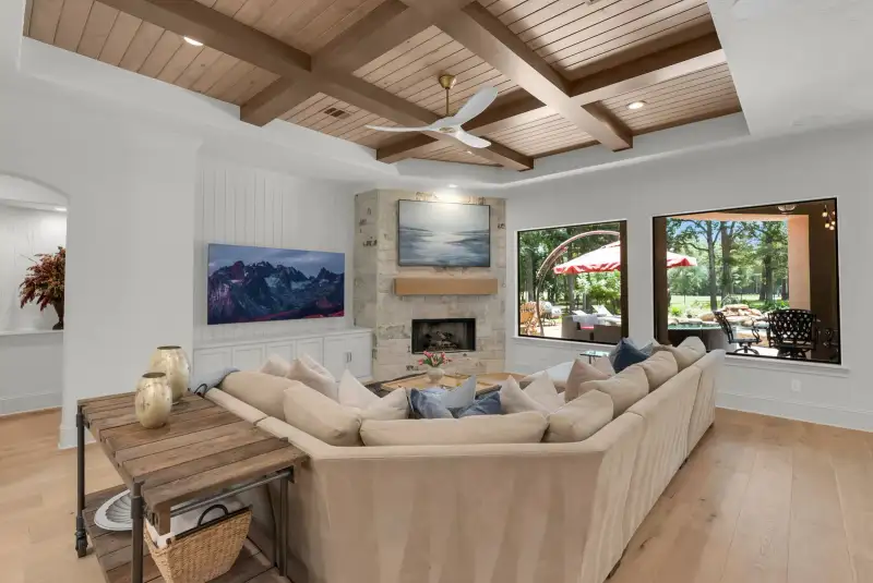 Living room with a coffered wood ceiling, a stone fireplace, a sectional sofa, and windows to a covered patio.