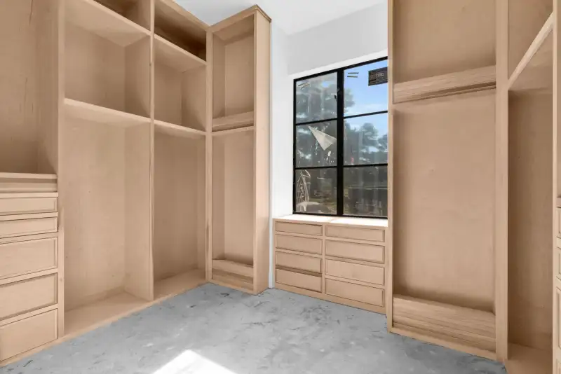 Walk-in closet with light wood shelving and drawers beneath a black-framed window.