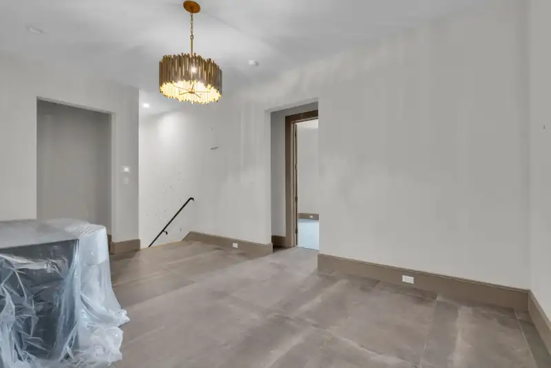 Room with a gold drum chandelier, gray tile floor, and an open doorway to a hallway.