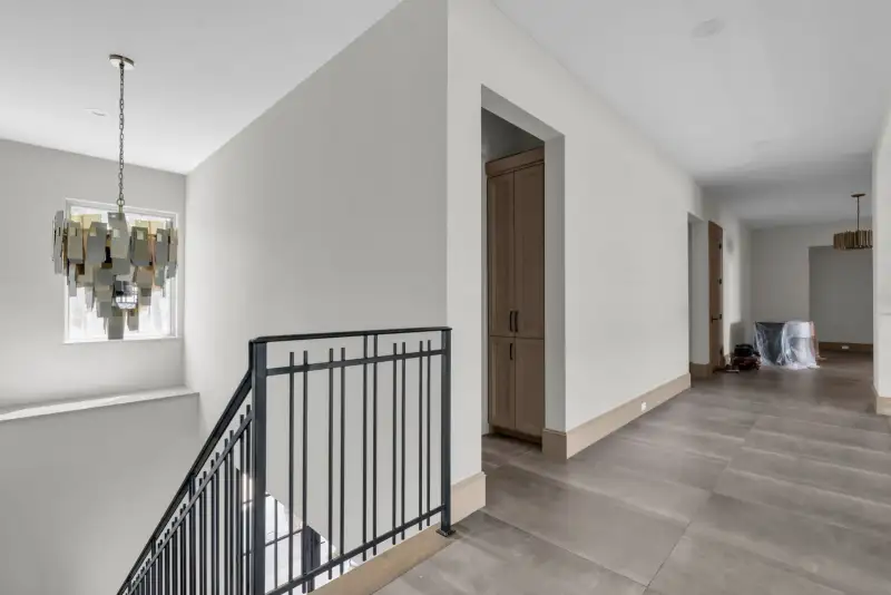 Upstairs hallway with a black metal stair railing, a chandelier, and a tile floor.