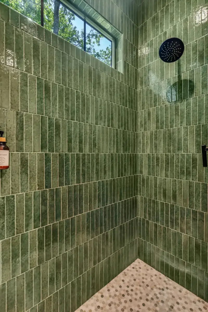 Shower with green vertical tile walls, a round rain showerhead, and a pebble-tile floor.