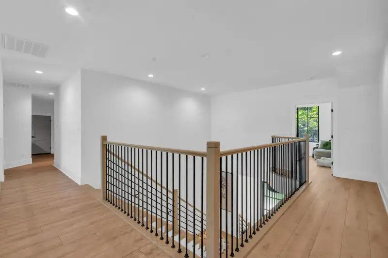 Upper landing with a wood railing and black metal balusters above the stairs.