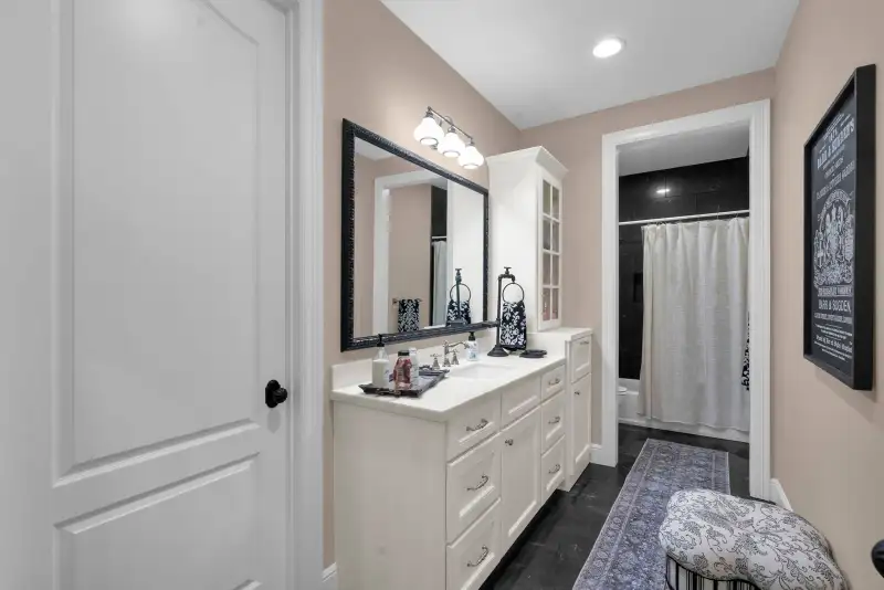 Bathroom with a white vanity, a framed mirror, a shower with a white curtain, and a dark tile floor.