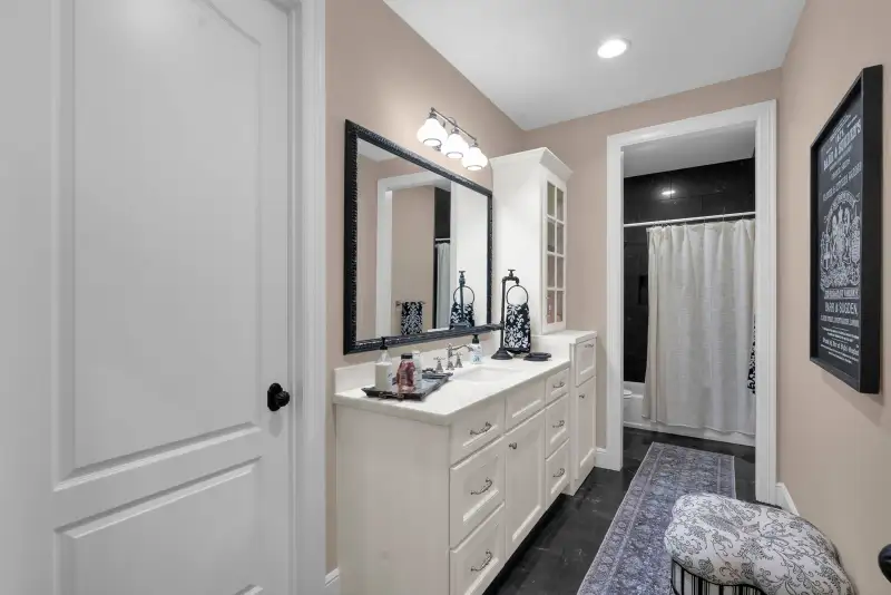 Bathroom with a white vanity, a framed mirror, a shower with a white curtain, and a dark tile floor.