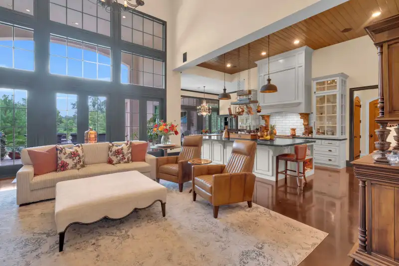 Great room with a cream sofa, leather armchairs, a white kitchen island, and a wood-plank ceiling.