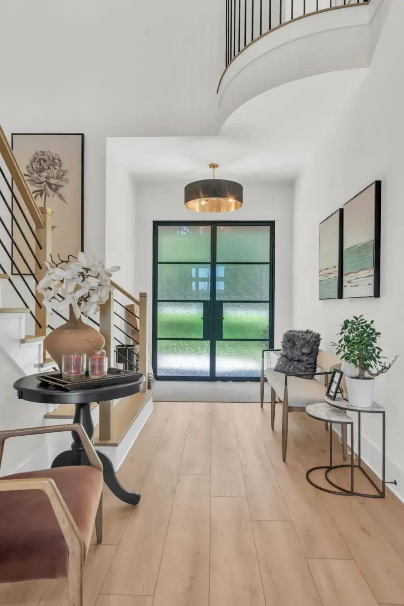 Entry foyer with a black-framed double door, a drum pendant light, and an armchair by a round side table.