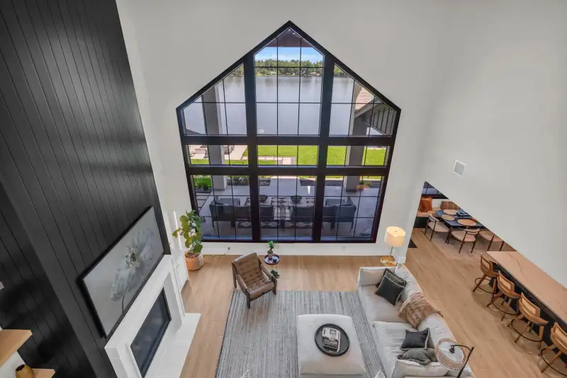 Living room below a tall gabled window, viewed from the upper landing, with a fireplace and gray sofas.