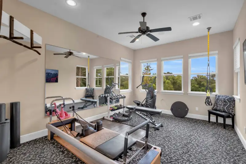 Home gym with a wall mirror, a reformer machine, an exercise bike, and a ceiling fan.