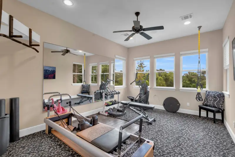 Home gym with a wall mirror, a reformer machine, an exercise bike, and a ceiling fan.