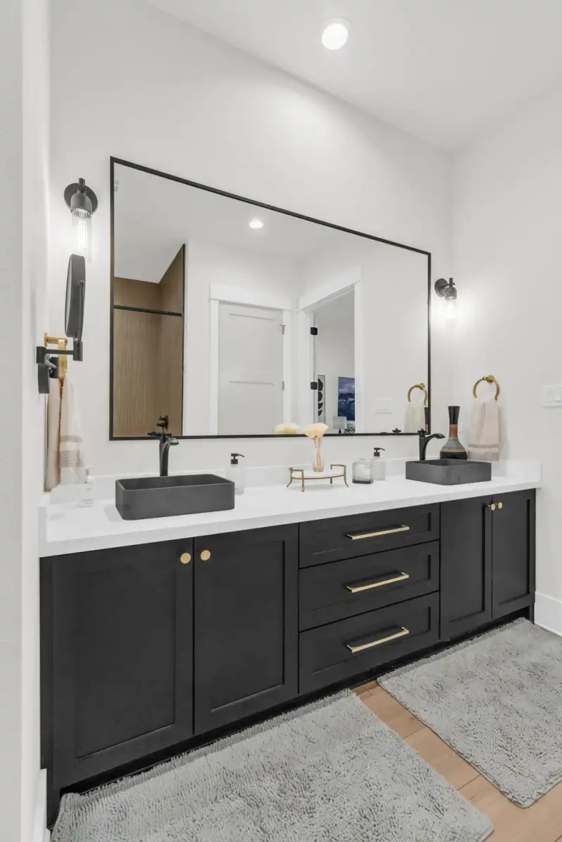 Double vanity with black cabinets, two gray vessel sinks, a framed mirror, and gold cabinet pulls.