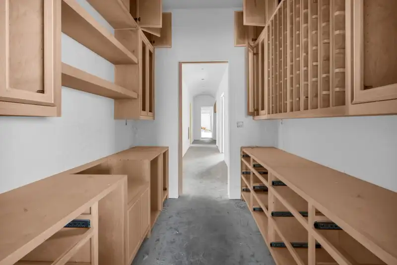 Pantry with wood cabinets and open shelves along both walls, with a doorway to an arched hall.