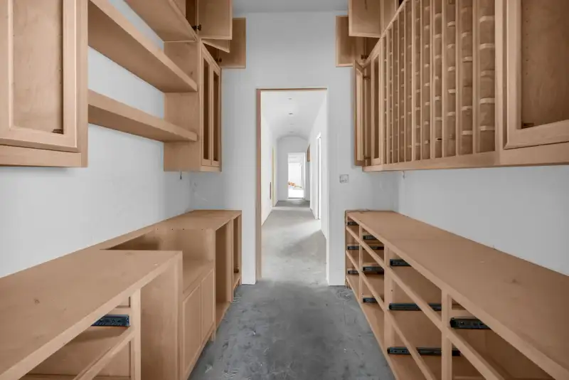 Pantry with wood cabinets and open shelves along both walls, with a doorway to an arched hall.