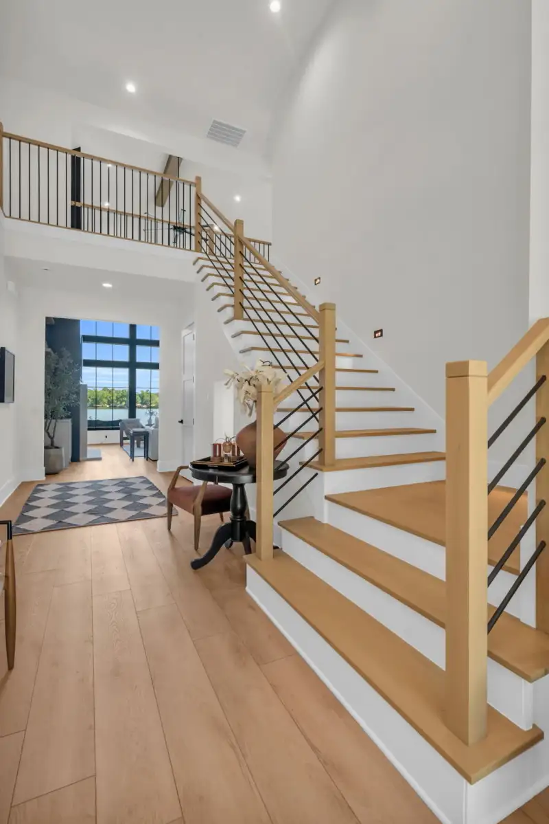 Foyer staircase with oak treads and black metal balusters above light oak flooring.