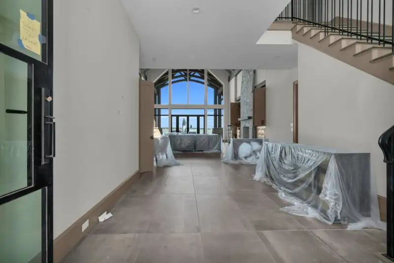 Entry hall with large gray floor tile, tall back windows, and a staircase at the right.