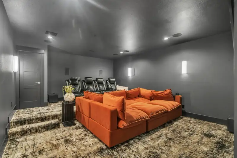 Media room with an orange sectional sofa, reclining theater seats, and a textured area rug.