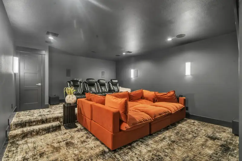 Media room with an orange sectional sofa, reclining theater seats, and a textured area rug.