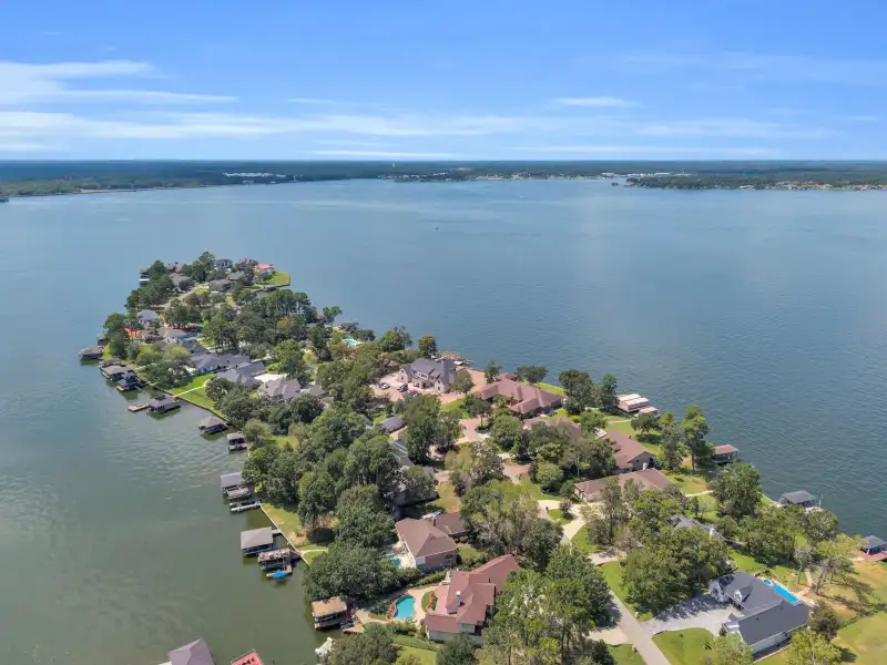 Aerial view of a lakeside point with homes, boat docks, and open water along the shoreline.