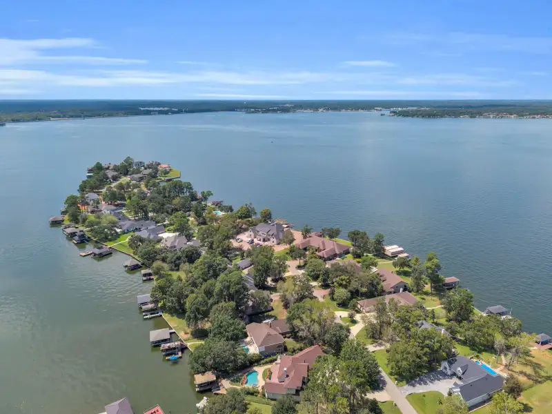 Aerial view of a lakeside point with homes, boat docks, and open water along the shoreline.