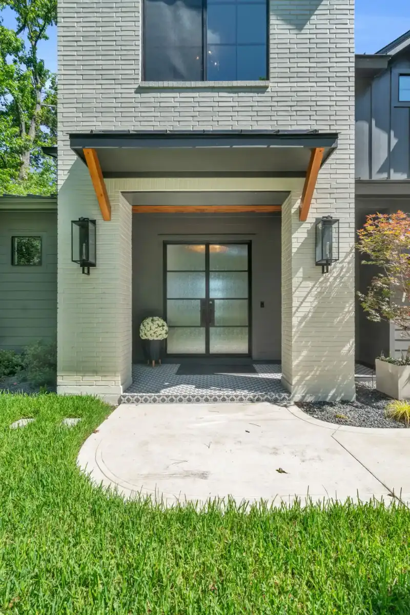 Front entry with a glass double door, wood brackets, and black wall lanterns on gray brick.
