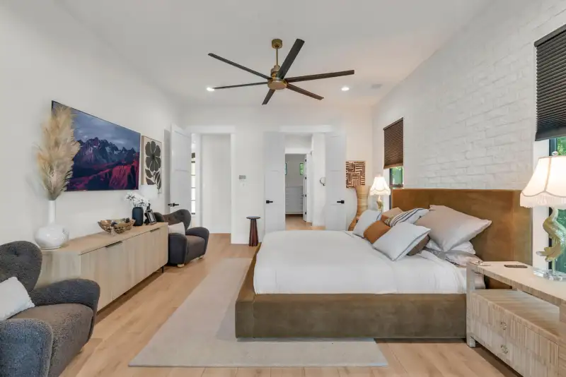 Bedroom with a ceiling fan, white brick accent wall, a large mountain photograph, and a brown upholstered bed.
