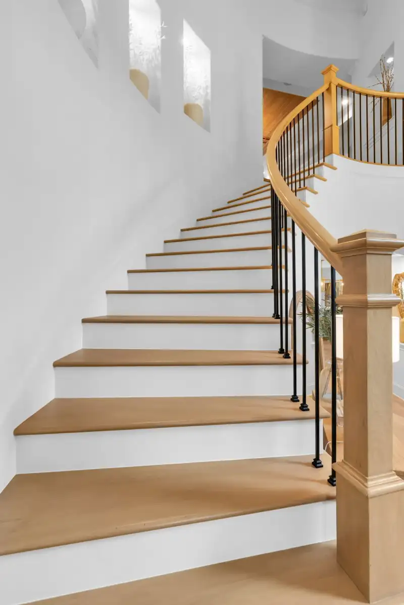 Curved staircase with light wood treads, black iron balusters, and a wood newel post.