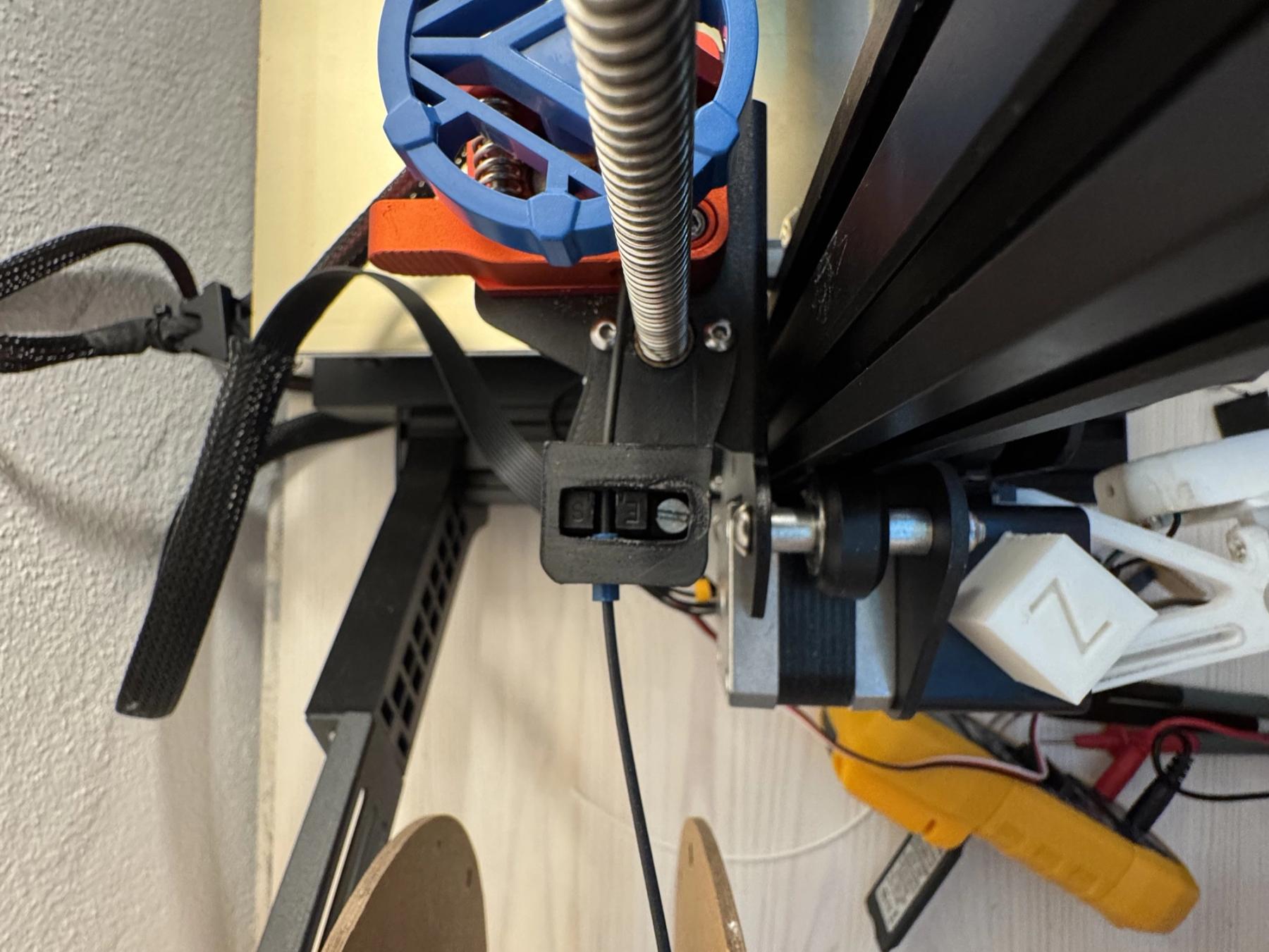 Installed 3D-printed optical filament sensor assembly on an Ender 3 V2, with the filament spool and guide hardware visible.