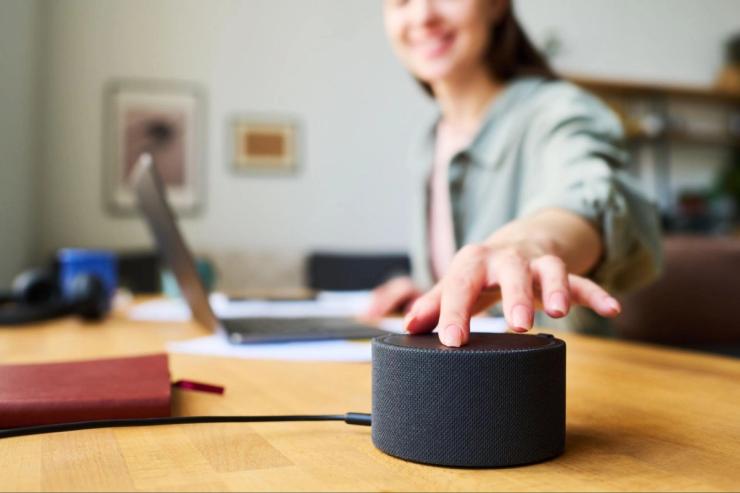 A woman at a desk touches a smart speaker device.