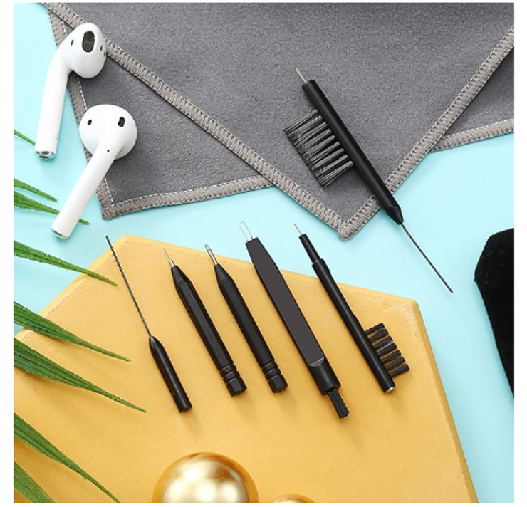 A hearing aid cleaning kit with brushes and cloths near some AirPods 