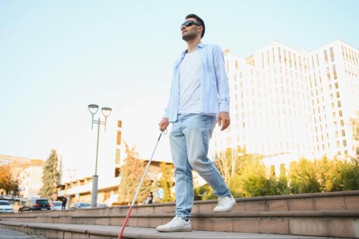 A blind man with a red and white cane walks down steps.